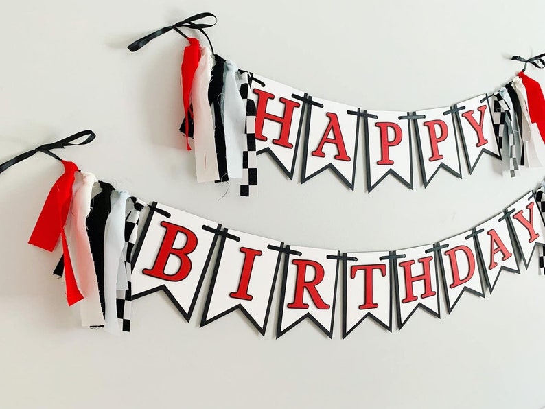 Op de afbeelding: Een wit-zwart geruit banner met rode letters die "Happy Birthday" lezen. De banner heeft zwarte en witte kwastjes die eraan hangen.