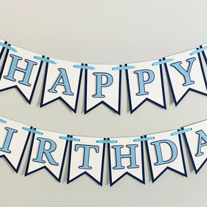 May include: A blue and white banner with the words "Happy Birthday" and blue tractor illustrations. The banner is strung together with blue ribbon.