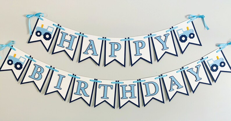 May include: A blue and white banner with the words "Happy Birthday" and blue tractor illustrations. The banner is strung together with blue ribbon.