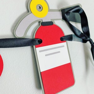 May include: A red and grey fire extinguisher paper craft with a yellow nozzle and black ribbon. The fire extinguisher has a white label with grey lines.