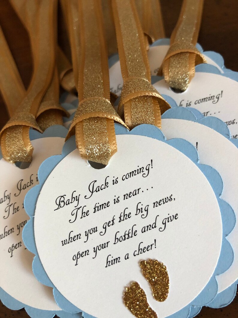 May include: Blue and white baby shower favor tags with gold glitter ribbon and gold glitter footprints. The tags read "Baby Jack is coming! The time is near... when you get the big news, open your bottle and give him a cheer!"