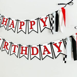 Op de afbeelding: Witte en zwarte banner met rode letters die "Happy Birthday" lezen. De banner heeft zwart-wit geblokt stof en rood-witte stoffen kwastjes.
