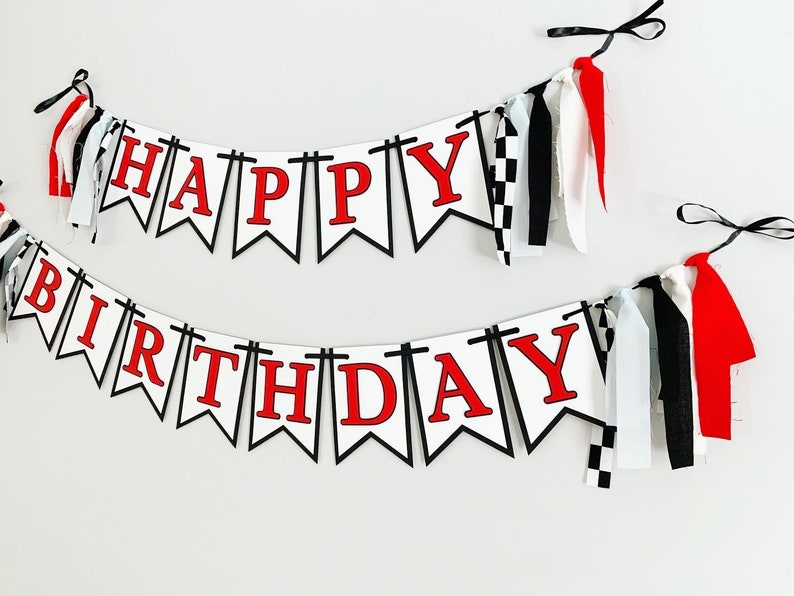 Op de afbeelding: Witte en zwarte banner met rode letters die "Happy Birthday" lezen. De banner heeft zwart-wit geblokt stof en rood-witte stoffen kwastjes.