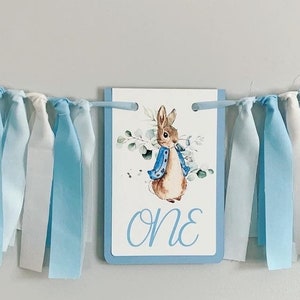 Peter Rabbit high chair banner featuring either a blue Peter Rabbit, pink Peter Rabbit, yellow Peter Rabbit or Green Peter Rabbit. The fabric will coordinate with the color of Peter Rabbit's jacket. The banner is available to read an age or name.