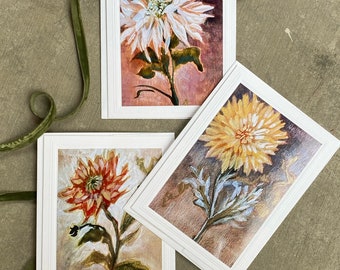 May include: Three white card stock greeting cards with a white border and a gold inner border. Each card features a watercolor painting of a single white, yellow, and red flower with green leaves on a brown background.