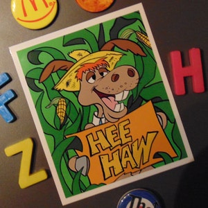 May include: A cartoon donkey wearing a straw hat and holding a sign that says "Hee Haw" in a green field with corn stalks.