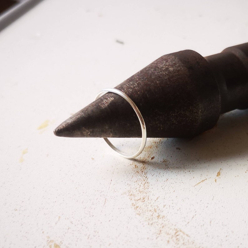 May include: A thin silver ring is being sized on a metal mandrel.