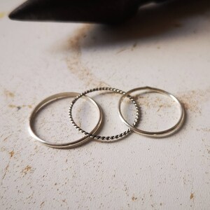May include: Three silver rings, one with a twisted design, on a white surface.