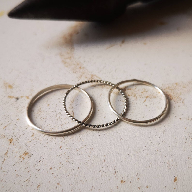 May include: Three silver rings, one with a twisted design, on a white surface.