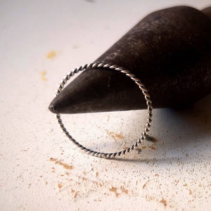 May include: A silver twisted wire ring, shown on a black metal surface.