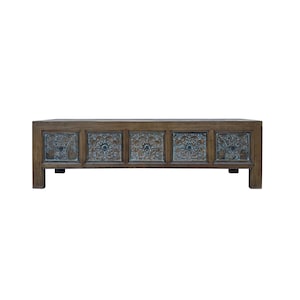May include: A rectangular wooden coffee table featuring five front-facing drawers. Each drawer front is decorated with a dark, intricate, embossed floral pattern and a small, centered circular metal knob. The table has a natural wood finish.