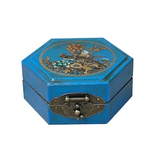 May include: A blue, octagonal jewellery box with a decorative bird and floral design on the lid. The box has a brass clasp and hinges. The artwork features a bird, flowers, and foliage in gold, green, and orange hues.