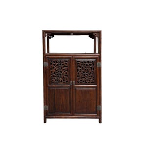 May include: A dark brown wooden cabinet with two doors and an open top shelf. The doors feature intricate carved floral designs. The cabinet has metal hinges and a rectangular shape, suitable for storage.