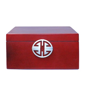 Puede incluir: Una caja de madera roja con un símbolo chino de metal plateado en la tapa.