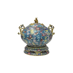 May include: A decorative, blue cloisonné vessel with a lid and base. The vessel features a detailed pattern of tigers, clouds, and floral designs in red, yellow, and white. The lid is topped with a small, gold-colored animal figurine.