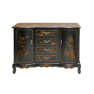 May include: A black wooden sideboard with ornate floral designs painted in gold. The sideboard has four drawers and two doors with decorative hardware. The sideboard has a curved top and sits on four legs.