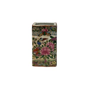 May include: A rectangular ceramic vase featuring a hand-painted floral pattern with pink peonies, green leaves, and a butterfly. The design includes a geometric border at the top and bottom, with a cream-colored background and gold-toned trim.