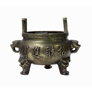 May include: A bronze incense burner with three legs and two handles. The burner has a round body with a raised rim and a textured surface. The burner is decorated with Chinese characters and dragon-like figures.