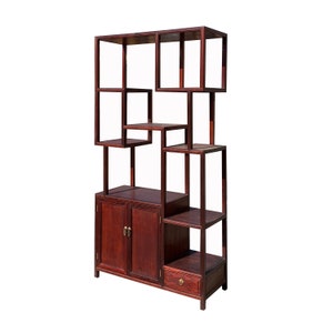 May include: A dark brown wooden shelf unit with a geometric design. The shelf has two doors, a drawer, and multiple open shelves.