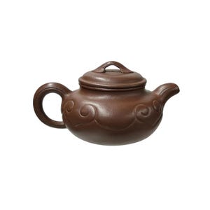 Könnte beinhalten: Eine braune Keramik-Teekanne mit Deckel und gebogenem Griff. Die Teekanne hat einen Ausguss und ist mit wirbelnden Mustern verziert. Die Teekanne ist zum Aufbrühen von Tee bestimmt.