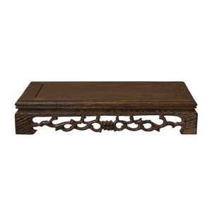 May include: A dark brown wooden plant stand with a rectangular top and an intricate carved design on the bottom shelf.