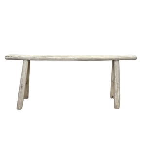 May include: A weathered, light-colored wooden bench with a rectangular seat and four angled legs. The bench appears to be made from a single piece of wood, with visible grain and natural imperfections. The bench is approximately 60 inches long.
