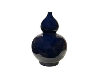 Op de afbeelding: Een donkerblauwe keramische vaas met een kalebasvorm. De vaas heeft een brede basis en een smalle hals.