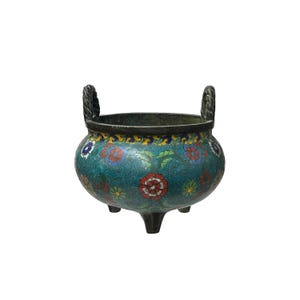 May include: A decorative, antique-style teal-colored bowl with a floral pattern in red, blue, and yellow. The bowl has two braided handles and three small feet. The rim is dark, and the overall design is ornate.