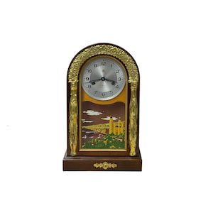 May include: An arched wooden mantel clock with a dark brown finish and gold-toned metal accents. The clock face is silver with black numerals and hands. Below the face is a colourful illustration of a bridge over water with green trees.