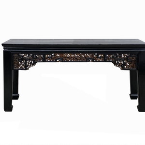 May include: A black wooden table with intricate carvings on the underside of the top. The table has a rectangular top and four legs.