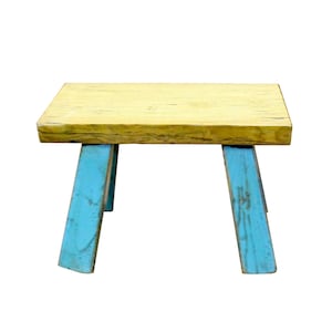 May include: A small wooden stool with a light yellow top and blue painted legs. The stool has a rustic, farmhouse style.