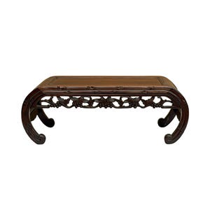 May include: A dark brown, low, rectangular wooden table with curved legs. The table features intricate floral carvings along the apron and a woven top. The table is designed to be a decorative piece.