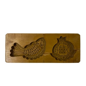May include: A wooden mold for making traditional Chinese pastries. The mold features two designs: a fish and a pomegranate with the Chinese character for "double happiness" carved into it.
