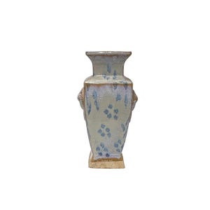 May include: A decorative vase with a rectangular base and a flared top. The vase is primarily light green with blue floral patterns and a textured surface. It has two decorative handles on the sides and measures approximately 10 inches in height.
