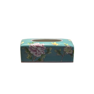 Op de afbeelding: Een turquoise keramische tissueboxhoes met een bloemenontwerp met roze en gele bloemen.