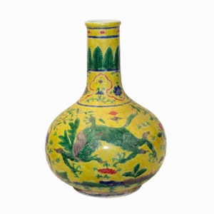 Peut inclure: Un vase en céramique jaune avec un corps large et rond et un long col étroit. Le vase est décoré d'un motif floral vert et bleu et d'une créature mythique verte.