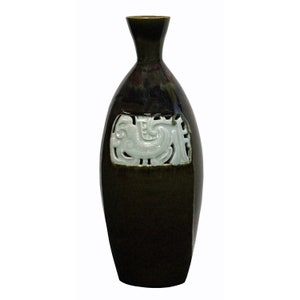 Könnte beinhalten: Eine dunkelgrüne Keramikvase mit einem weißen, geschnitzten Design auf der Vorderseite. Die Vase hat einen schmalen Hals und einen runden Körper.
