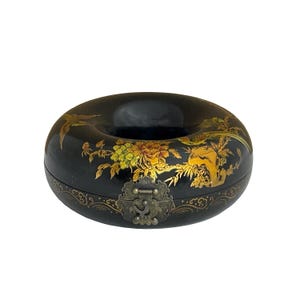 May include: A black, donut-shaped decorative box with a hinged lid and clasp. The box is adorned with gold floral and bird designs. The box has a dark interior and a decorative border around the base.