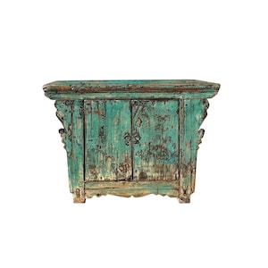 May include: A distressed teal blue wooden cabinet with two doors and ornate carvings. The cabinet has a weathered finish and is a vintage style.