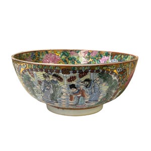 May include: A large, round, porcelain bowl with a gold rim and intricate hand-painted floral and figural designs in shades of pink, blue, green, and gold. The bowl features a scene of people in traditional Chinese clothing.