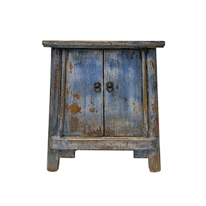 May include: A small, blue and brown wooden cabinet with two doors and antique-style hardware. The cabinet has a distressed finish and sits on four short legs.