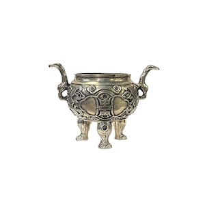 May include: A silver incense burner with intricate carvings and three legs. The burner features a double happiness symbol in the center.