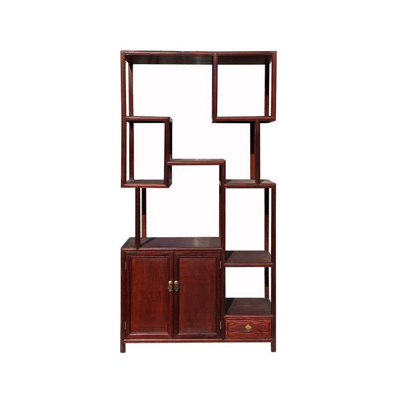 May include: A dark wood bookshelf with a unique asymmetrical design. It features multiple shelves, two doors, and a drawer. The doors have brass handles.