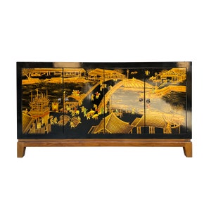 May include: Black lacquered cabinet with four doors featuring a gold painted scene of a Chinese village with a bridge and boats. The cabinet has a wooden base with four legs.