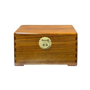May include: A rectangular wooden box with a polished finish. The box features a decorative brass clasp and hinges. The wood grain is visible, and the box has a traditional design. The box is likely used for storage.