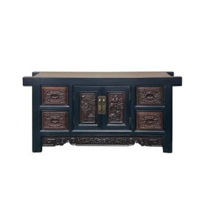 May include: A dark blue wooden cabinet with carved floral and geometric designs. The cabinet has two doors and four drawers with brass hardware. The top is a lighter brown color.