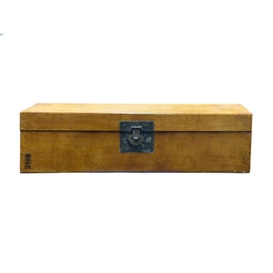 May include: A rectangular wooden storage box with a smooth, light brown finish. The box features a dark, weathered metal latch centered on the front panel and a small, black stamped character mark on the lower left corner of the front face.