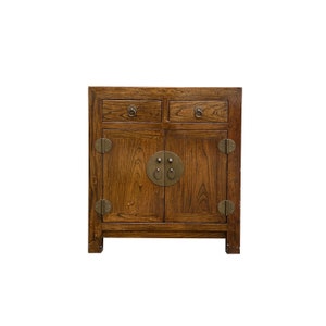 May include: A dark brown wooden cabinet with two drawers and two doors. The doors have brass hardware with circular designs. The cabinet has a simple, traditional style.