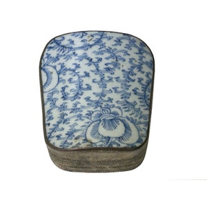 Puede incluir: Una pequeña caja rectangular con una tapa de porcelana azul y blanca. La tapa presenta un patrón floral con un diseño delicado.