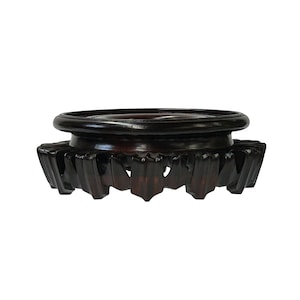 May include: A dark brown wooden pedestal with a round top and a scalloped base. The pedestal is designed to display a vase or other decorative object.